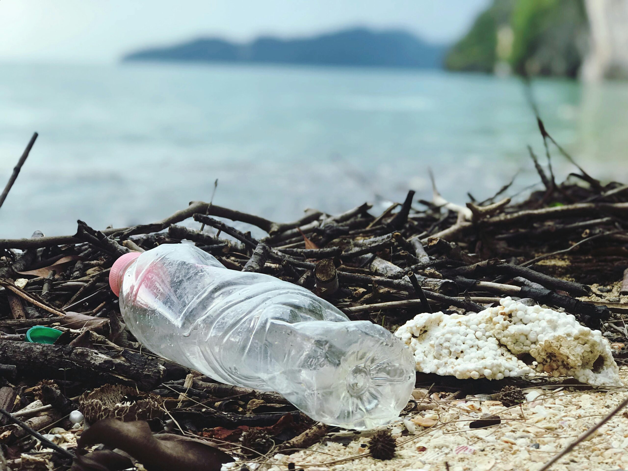 plastic water bottle laying next to body of water. Embracing the benefits of using a reusable water bottle.