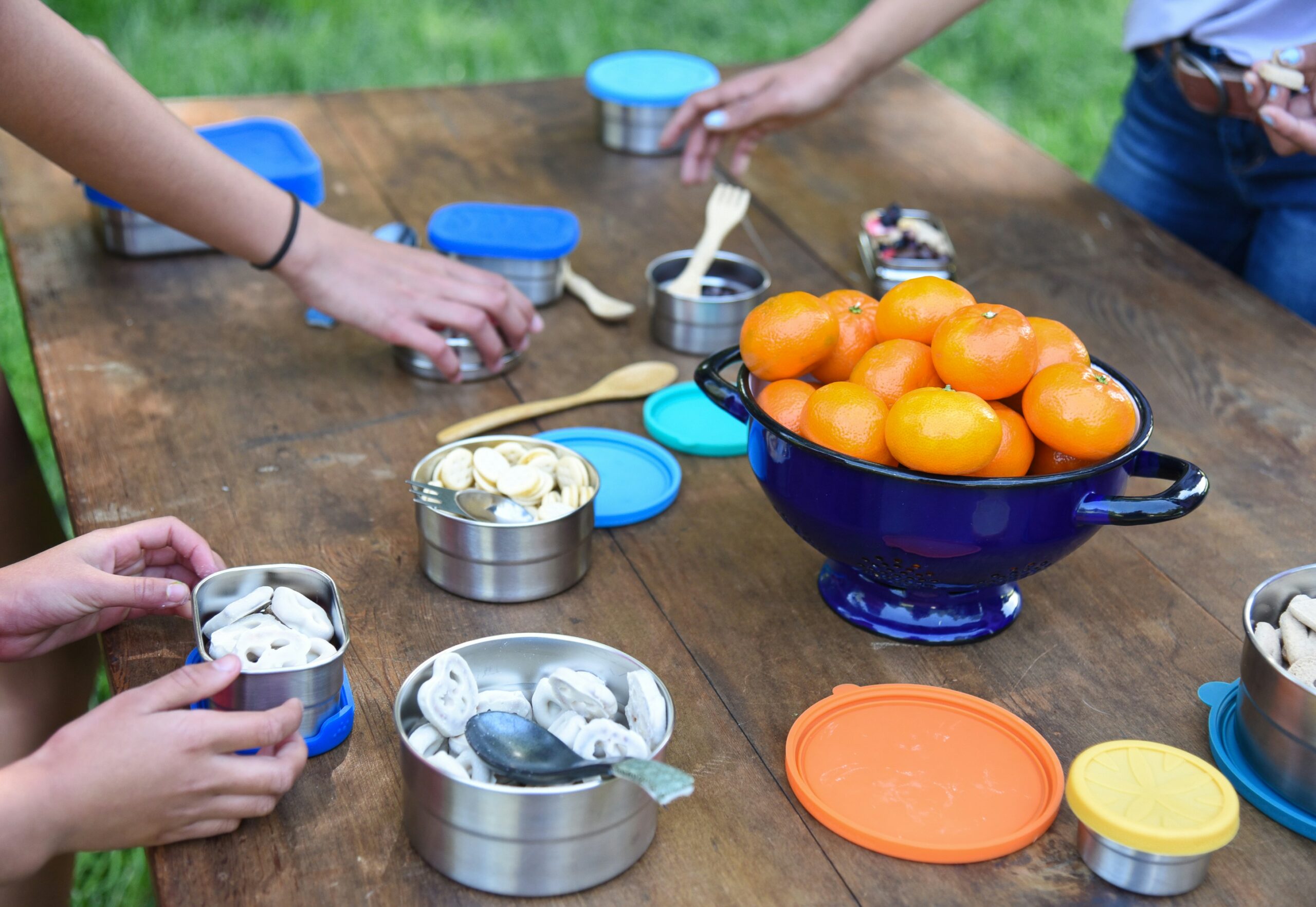 Food items in stainless steel and sustainable containers on an outdoor table. 