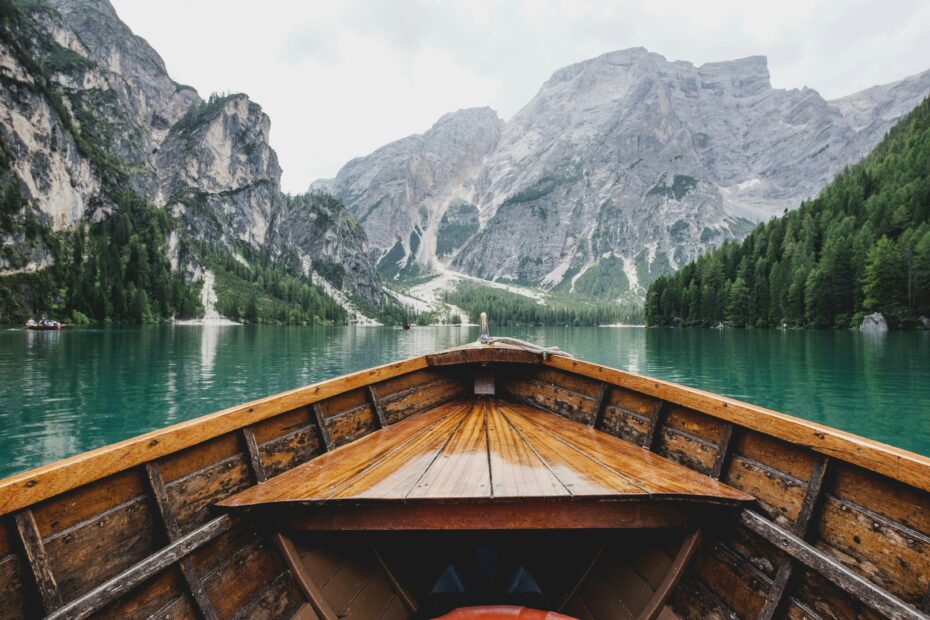 a wooden boat floating down a river with beautiful scenic background of mountain and trees