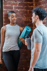 male and female talking at gym. Female holding yoga mat and male holding eco-friendly sustainable water bottle