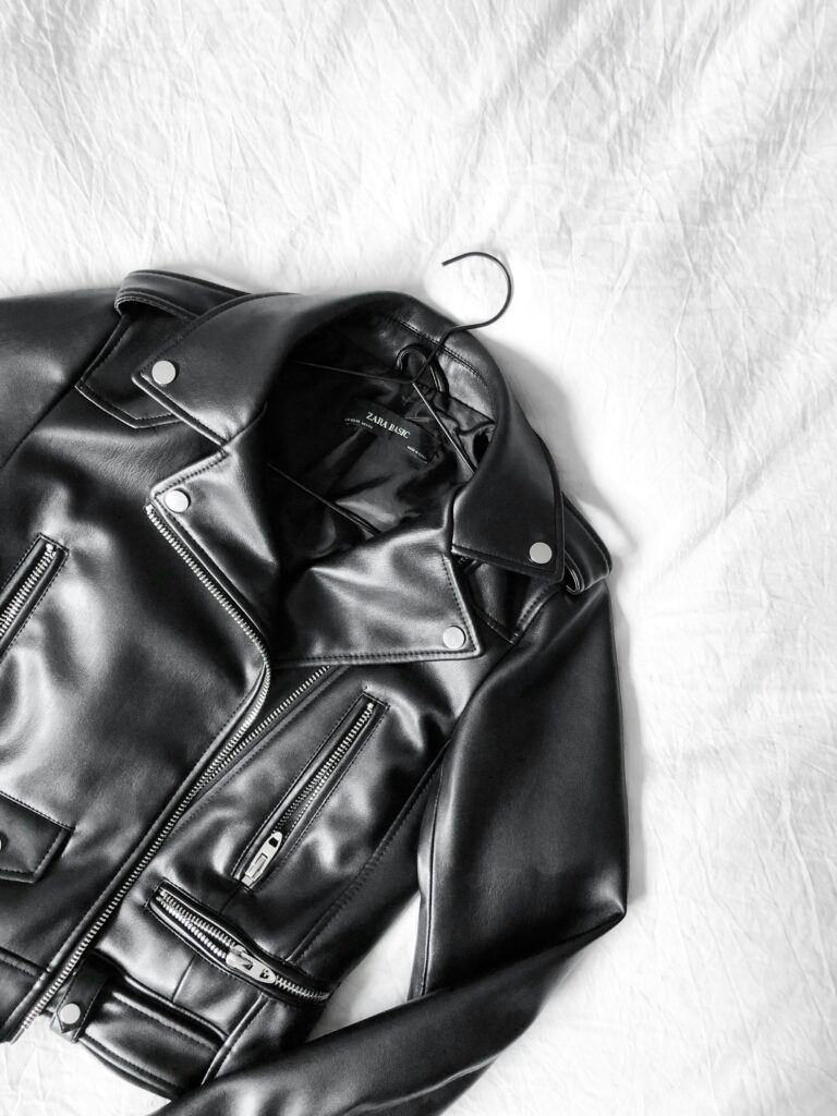 black leather jacket laying down on display with the hanger still in position inside the jacket